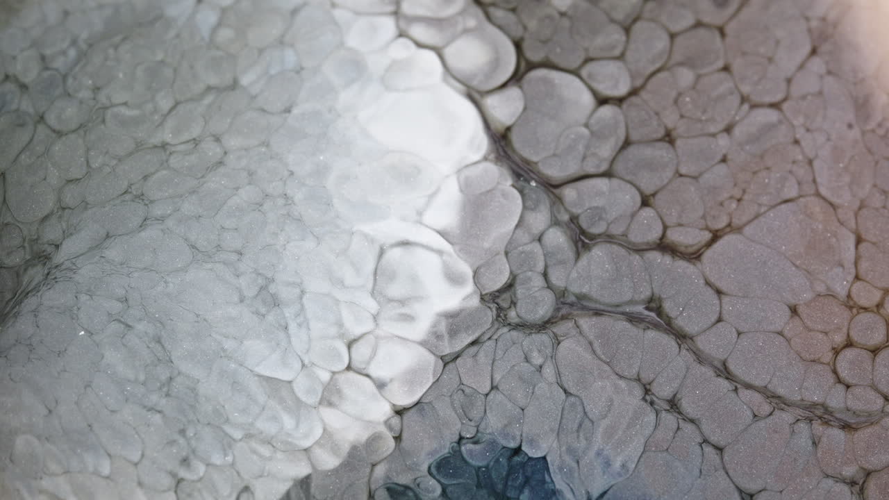 Dark liquid drips and spreads on a white surface creating abstract patterns in slow motion