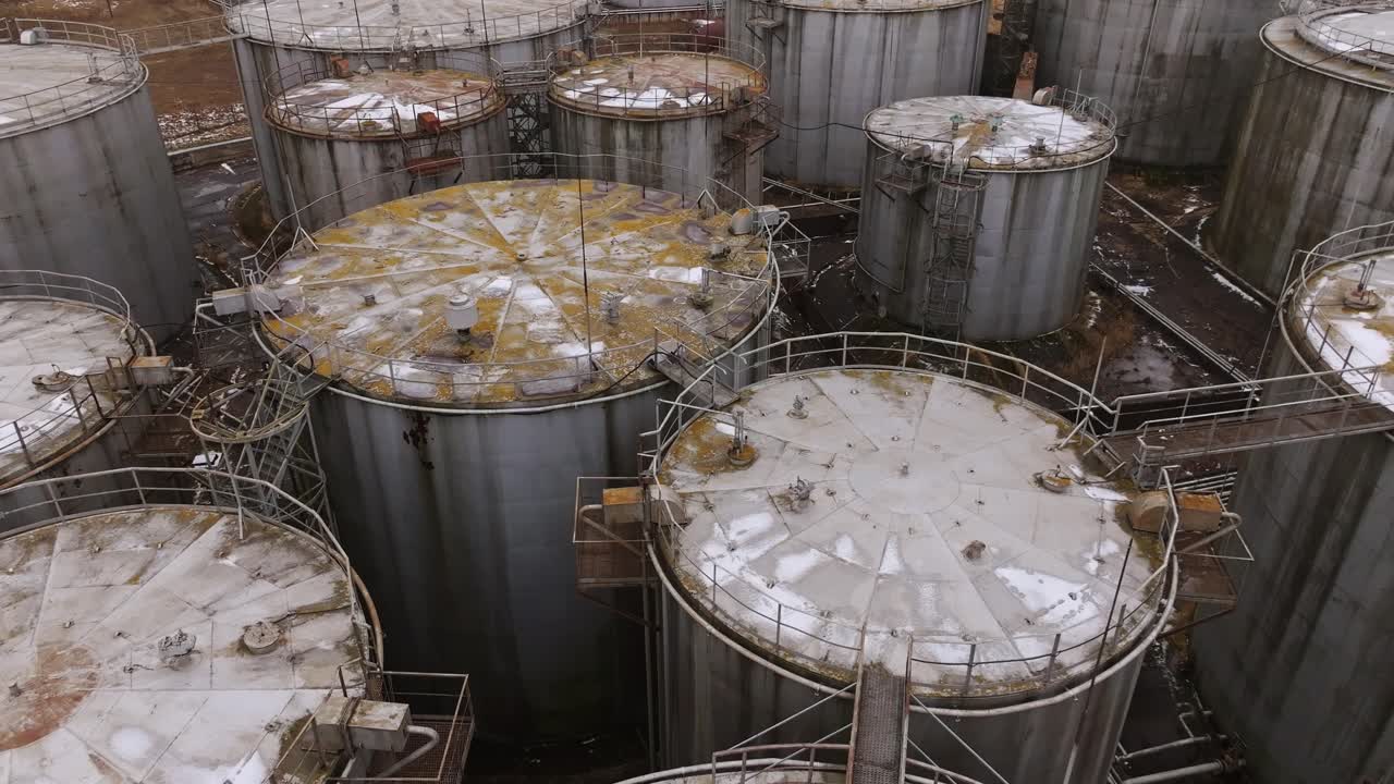 Decaying industrial storage facility, rust-stained tanks, corroded metal, drone