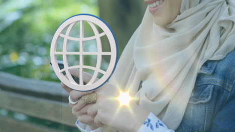 Using smartphone, woman in hijab with globe icon and bright animation light