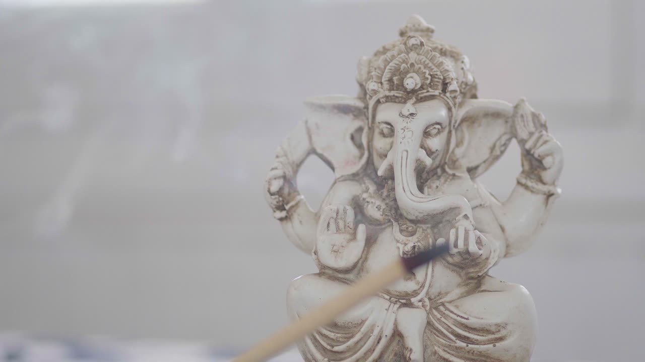 primer plano de una estatuilla de ganesha detrás de un incienso ardiente
