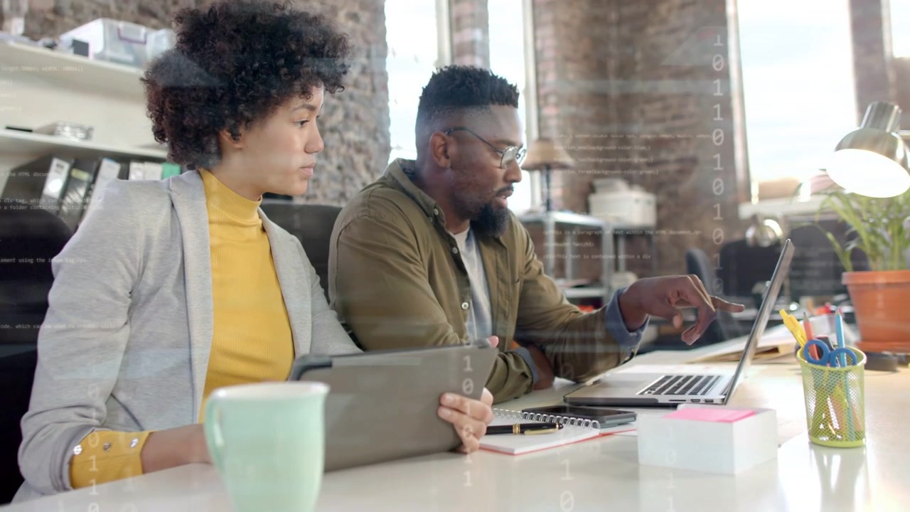 Man tapping laptop, binary overlay rising while woman scanning tablet confirming business KPIs