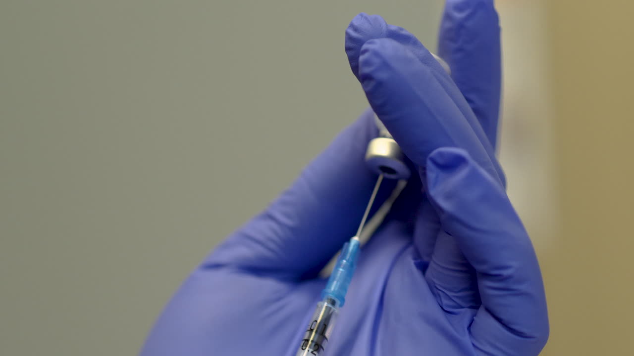 The doctor in protective gloves holds a syringe and a vaccine bottle for coronavirus treatment