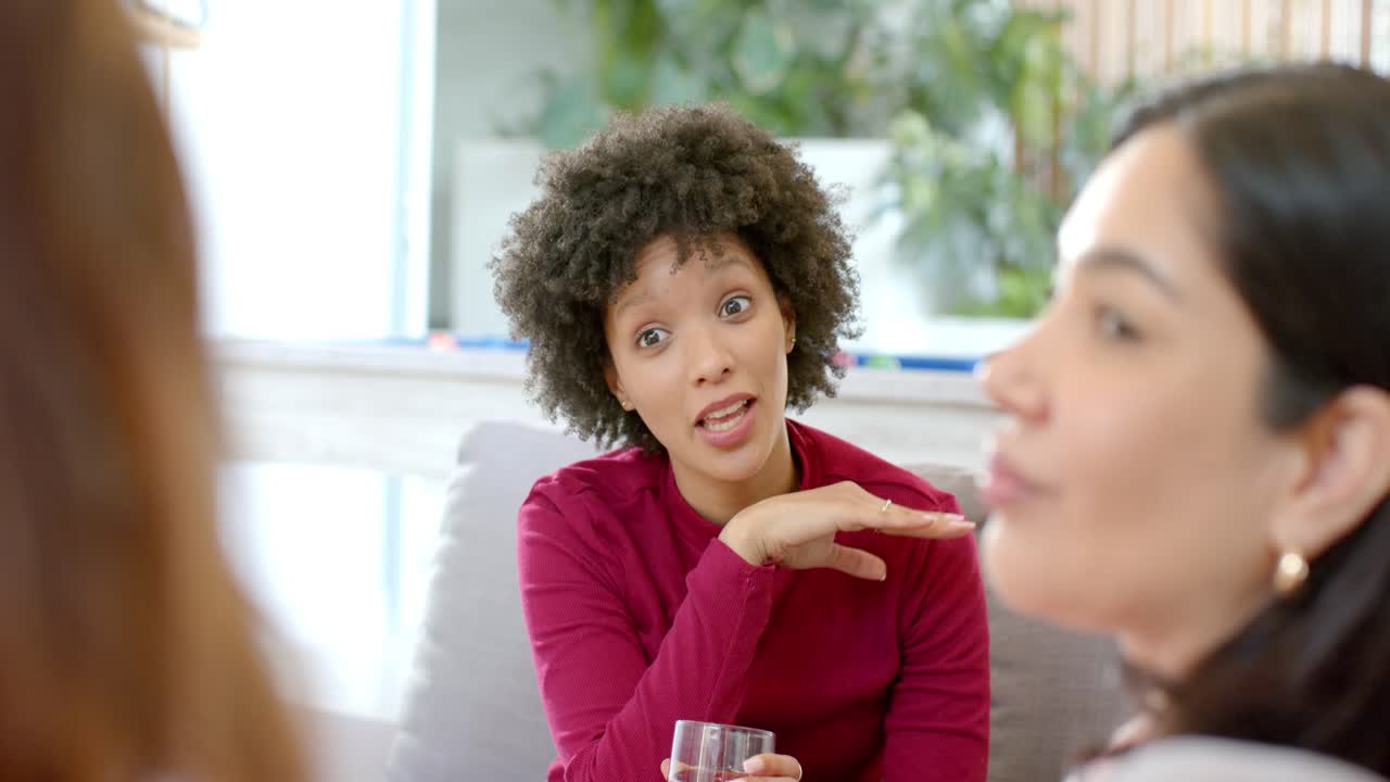 Donna adulta che tiene un bicchiere e indica mentre spiega un'idea sul divano del soggiorno con cuscini.