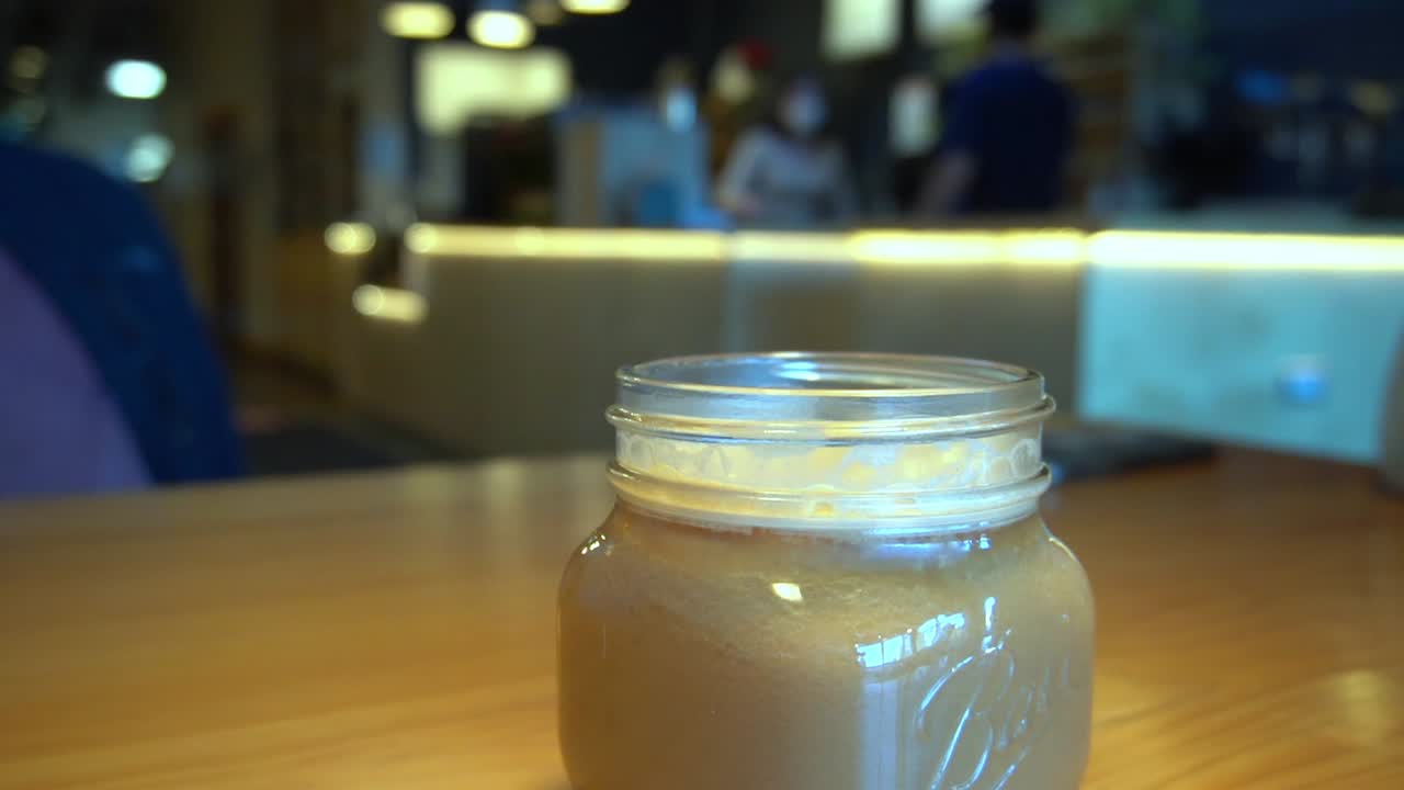 복면을 쓴 직원이 마스크를 쓴 고객의 주문을 받는 커피숍의 3-3 보케 배경과 코비드 제한 기간 동안 흐릿한 사람들이 앉아 술을 마시는 항아리 모양의 커피 음료가 있는 전경