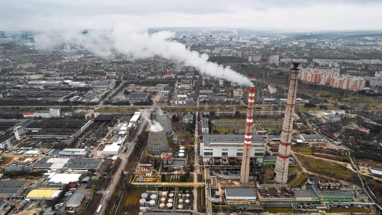 Aerial drone timelapse view of thermal power plant in Chisinau at cloudy weather, Moldova. View of pipes with felling steam, buildings and yellowed trees around