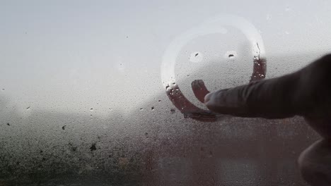 Hand-drawing-smiling-face-on-window-glass-with-condensation