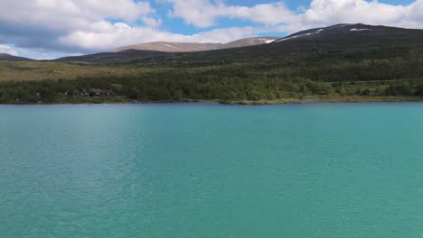 vista aérea del sereno lago turquesa en el telón de fondo de una exuberante ladera verde bajo un cielo azul parcialmente nublado, capturando la esencia de la tranquilidad y la belleza natural