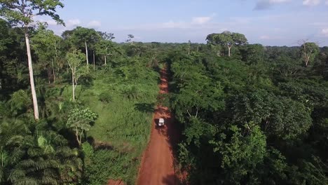 Video-Desde-Lo-Alto,-El-Dron-Vuela-Hacia-Adelante-Mientras-Sigue-A-Un-Vehículo-Todoterreno-Blanco-A-Través-Del-Camino-De-Tierra-Que-Fluye-A-Través-Del-Bosque