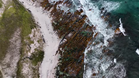 aerial birdseye view of dramatic rocky coast with green water crashing on brown and white sands beach