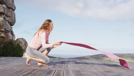 Caucasian-woman-laying-out-yoga-mat-outdoors-on-deck-in-rural-mountainside-setting