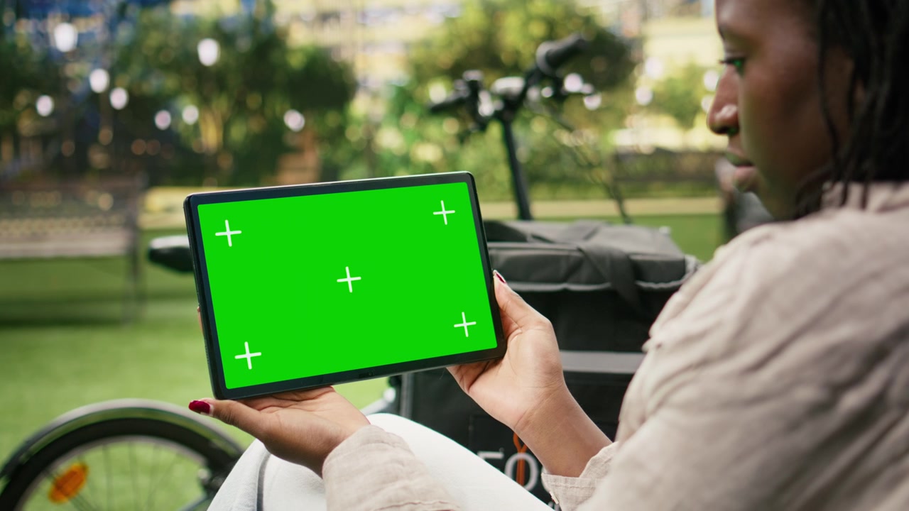 Green screen chroma key su display di tablet tenuto da una donna corriere in un parco cittadino