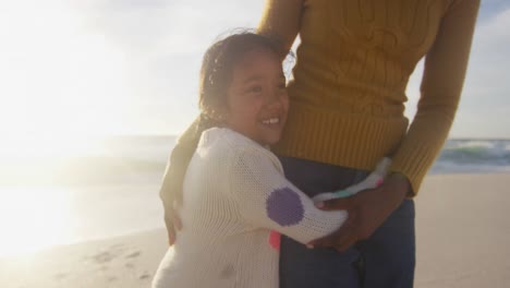 feliz hija hispana abrazando a su madre en la playa al atardecer