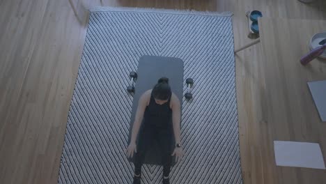 an overhead static shot of a women doing sit ups in the living room of her home