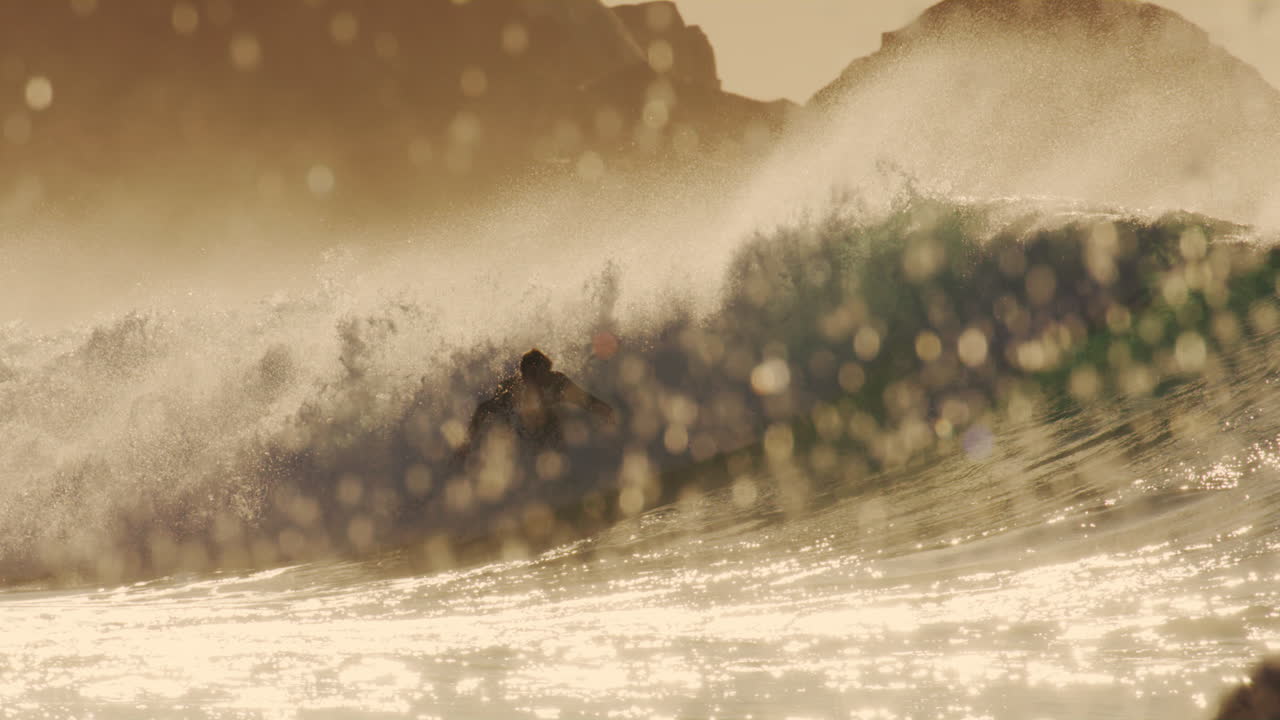Golden glassy wave with surfer kicking back and spraying out across water at sunset, silhouette