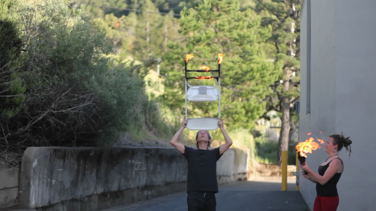 불타는 횃불을 저글링하면서 이마에 불타는 의자를 올려 놓고 균형을 잡는 거리 공연가의 기술