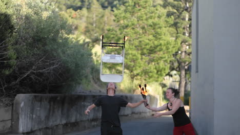 a street performer displays his skills by balancing a flaming chair on his forehead while juggling flaming torches