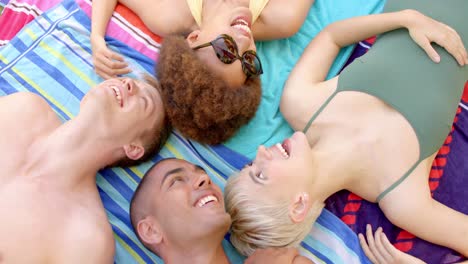 happy diverse group of friends lying on towels in summer