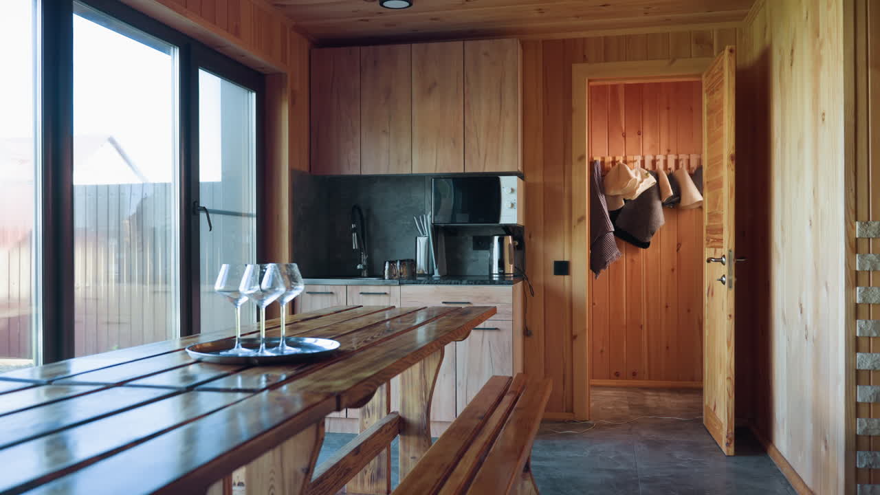 large cozy cabin kitchen with wooden walls and cabinets, bench table, microwave, kettle, fireplace, sliding glass door with natural light, modern rustic interior blending wood and stone