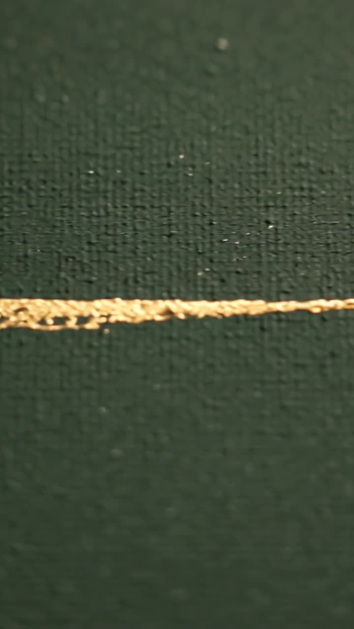 Vertical video: Camera zooming showing gold braided thread on dark green cloth to inspect knot