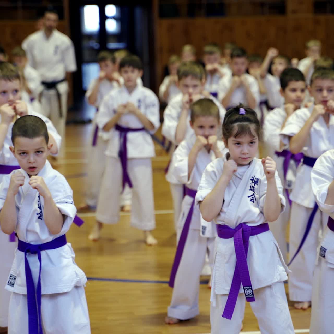 Teenage karate kids practicing diverse moves during training. Adult trainers walk along the rows and watch the students. Blurred backdrop