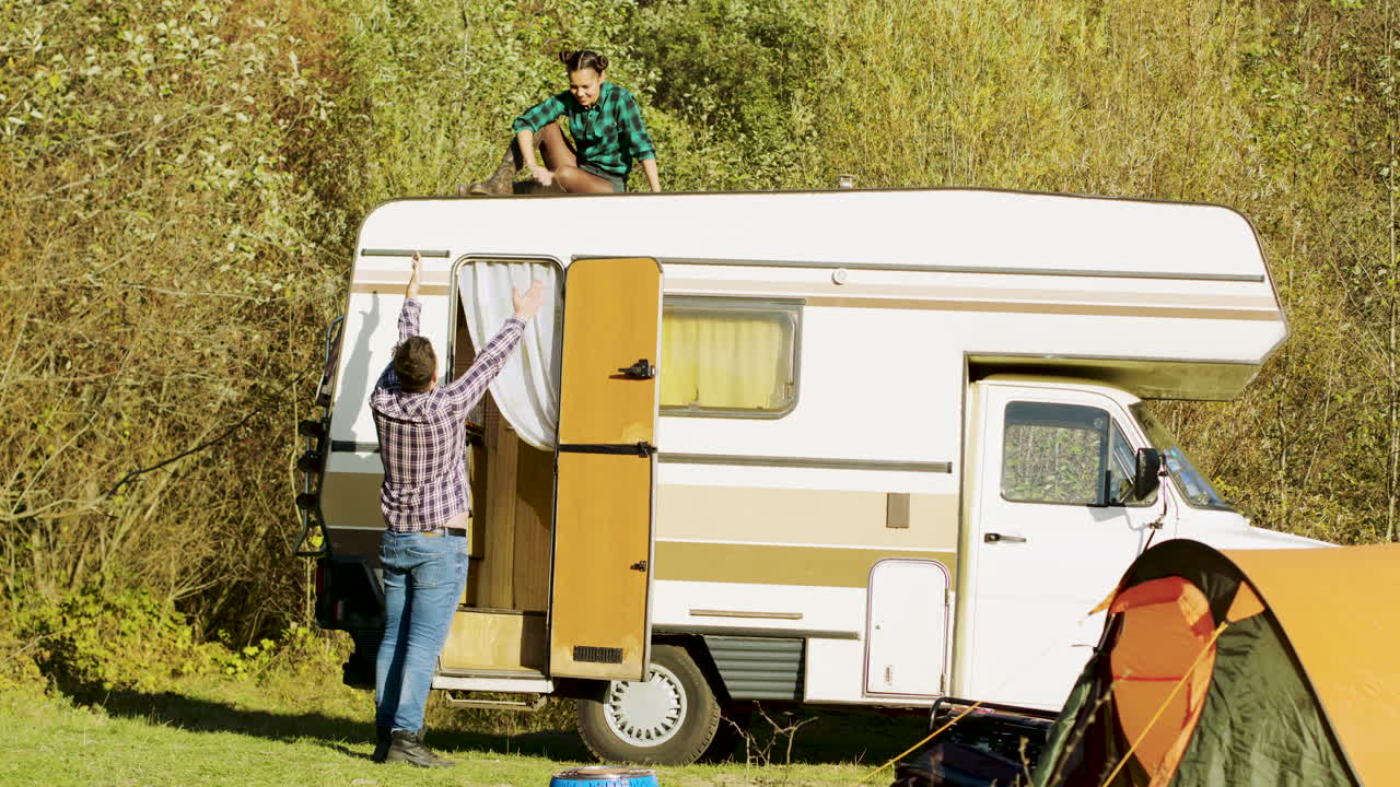 Boyfriend saying hello to her girlfriend who's relaxing on top of their vintage camper van