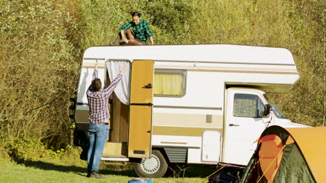 boyfriend saying hello to her girlfriend who's relaxing on top of their vintage camper van