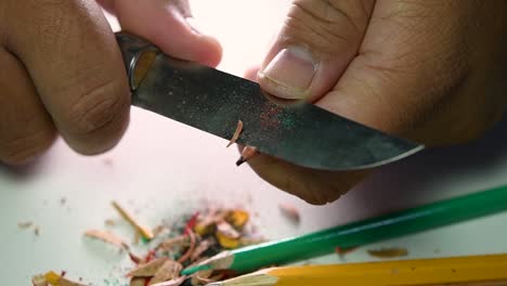 footage of hands slowly sharpening a pencil and some coloured pencils with a sharp knife