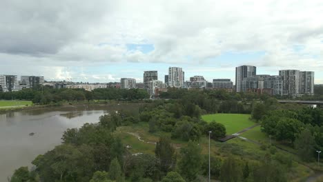 Vuelo-Aéreo-Sobre-Un-Hermoso-Parque-Verde-Y-Un-Río-Con-Paisaje-Urbano-En-El-Suburbio-De-Sydney,-Australia