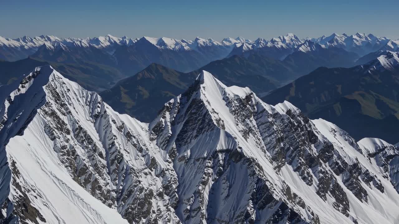 Aerial video captures majestic snow-capped mountain peaks with sharp ridges, offering a breathtaking