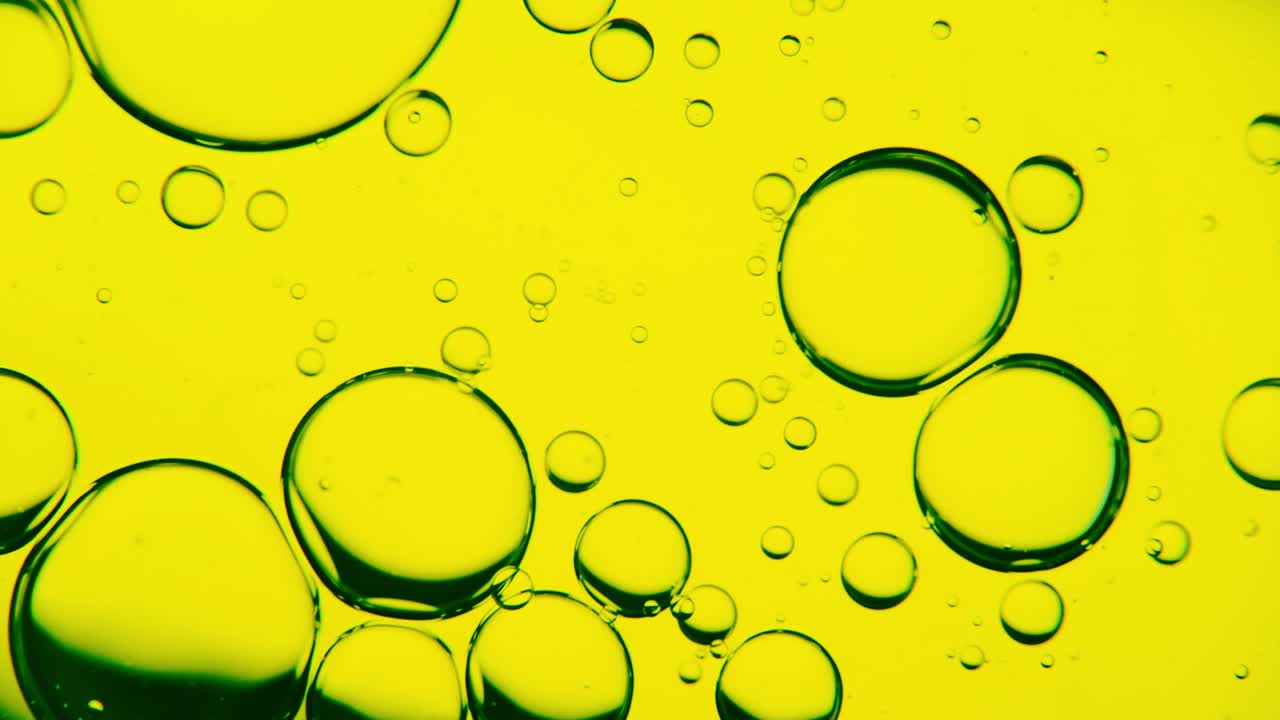 burbujas de aceite en movimiento en la superficie del agua, sobre un fondo amarillento-verde, macro, pantalla de inicio, plantilla, espacio de copia