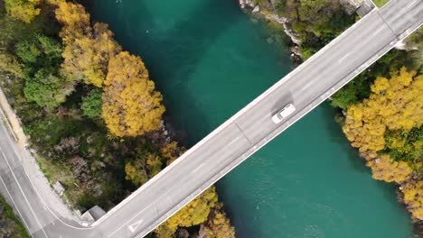 aerial top down rising shot of cars on the bridge crossing the river, autumn colours