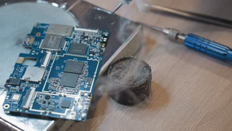 a close-up view of a soldering iron in action, with a technician working on a blue printed circuit board, with screw on the table and other tools