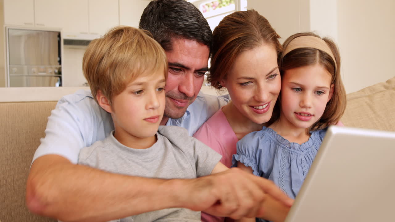 Famiglia giovane e felice seduta sul divano che usa il laptop insieme
