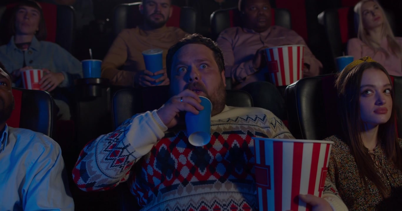 Uomo che mangia popcorn e beve una bibita al cinema