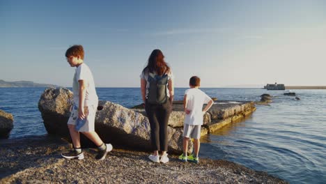 Caucasian-mother-and-her-two-boys,-enjoying-a-walk-on-a-rocky-pier-at-Kalamata-port,-during-golden-hour,-medium-static-shot-4K