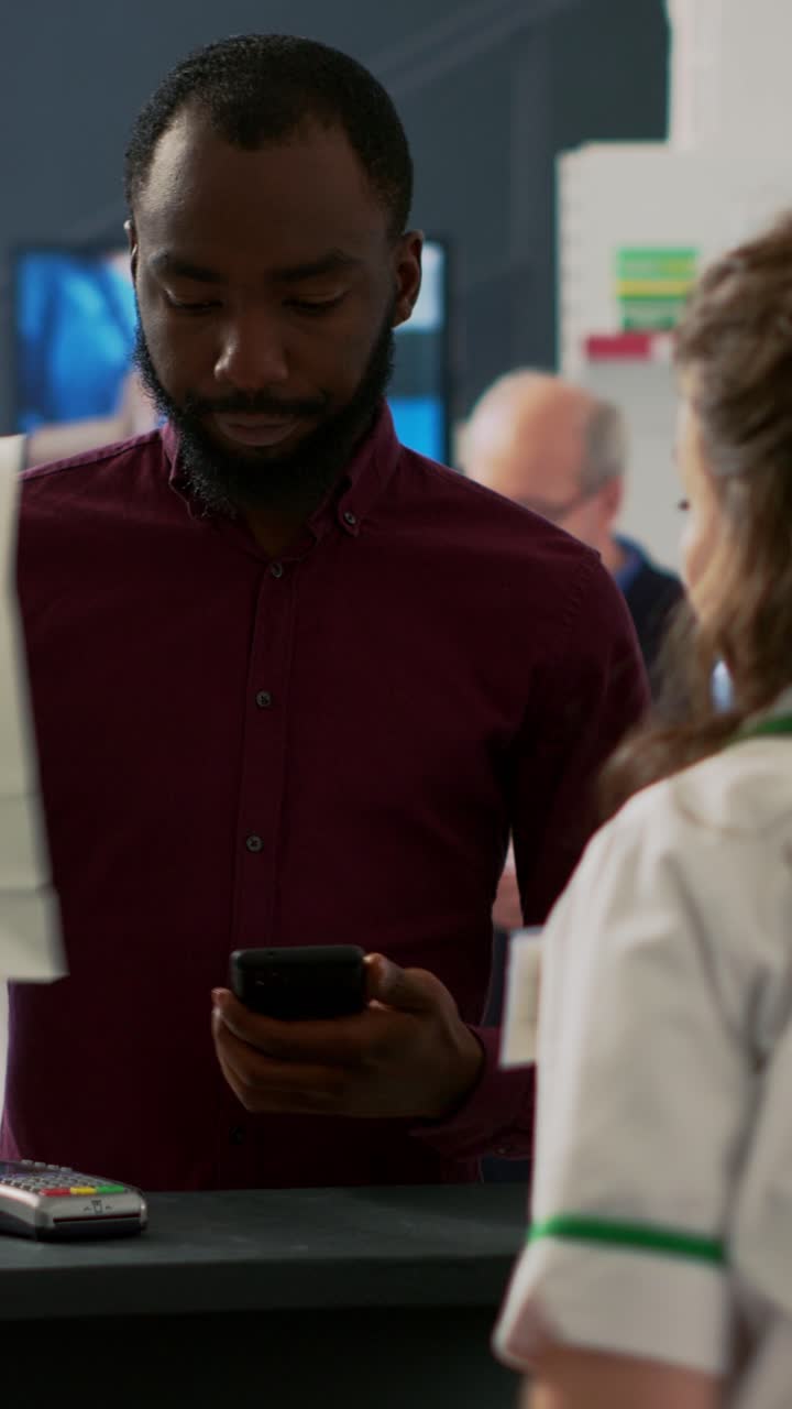 Vertical video: African american client using nfc mobile payment to buy supplements