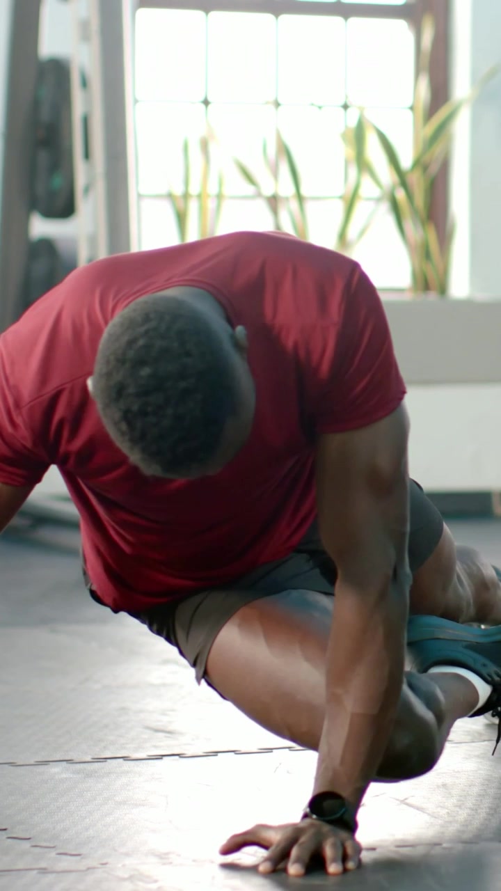 Video verticale: Uomo in maglietta rossa che inizia un plank alto, alternando le ginocchia incrociate sul corpo su un tappetino da palestra per gli addominali.