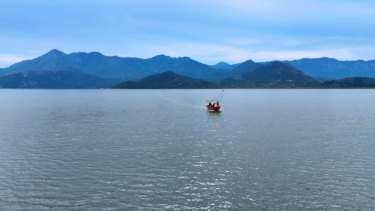 Ulcinj, Montenegro, 14 August 2025: Small boat on lake horizon. A small boat heads across the lake horizon with tall mountains rising behind