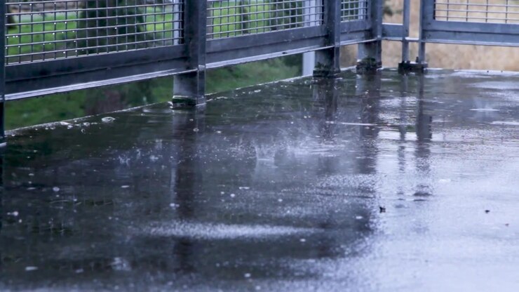 rain splatters into puddles on concrete near a metal fence
