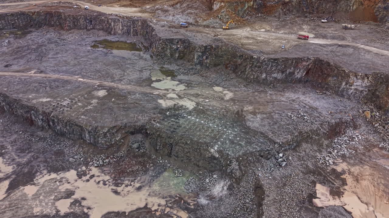 Sito di cava di granito che mostra un'ampia area di scavo con veicoli e attrezzature in funzione durante le ore diurne.