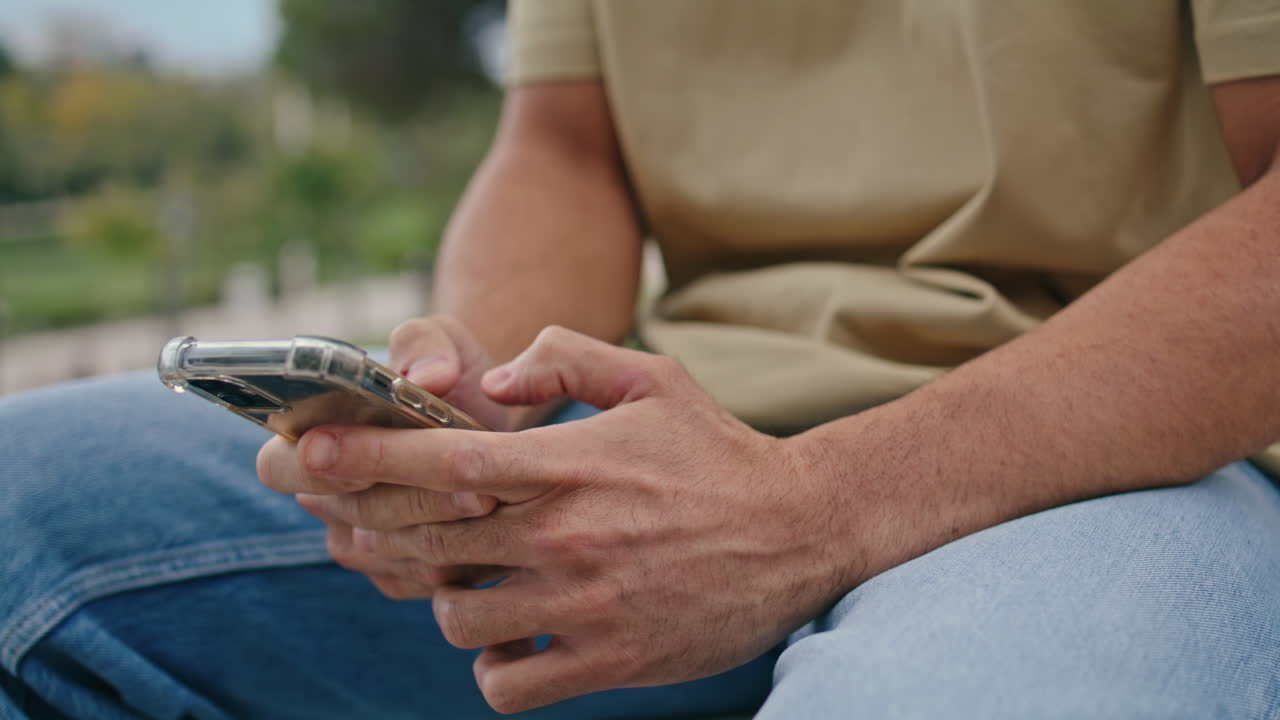 Mani di un uomo messaggiano al cellulare all'aperto, in primo piano. Uomo sconosciuto che scrive un messaggio.