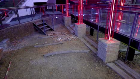 a construction area with neon red lighting inside a museum in bangkok. the environment is industrial with visible debris and glass barriers