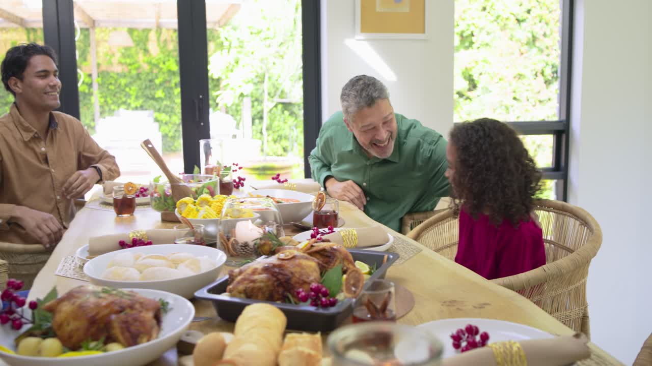 Diverse family bowing heads in gratitude then passing turkey at dining table to begin meal