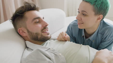 pareja joven tumbada en el sofá hablando y acariciándose