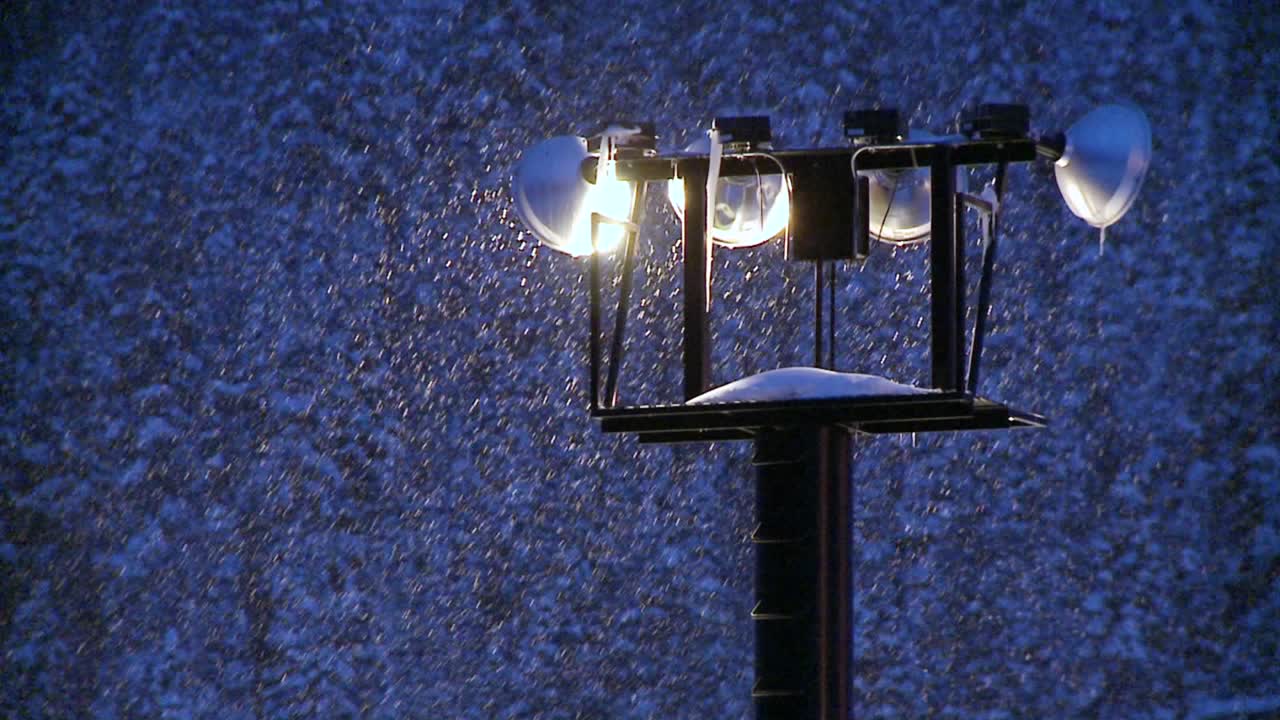 빛나는 투광 조명을 통해 밤에 눈이 내립니다.