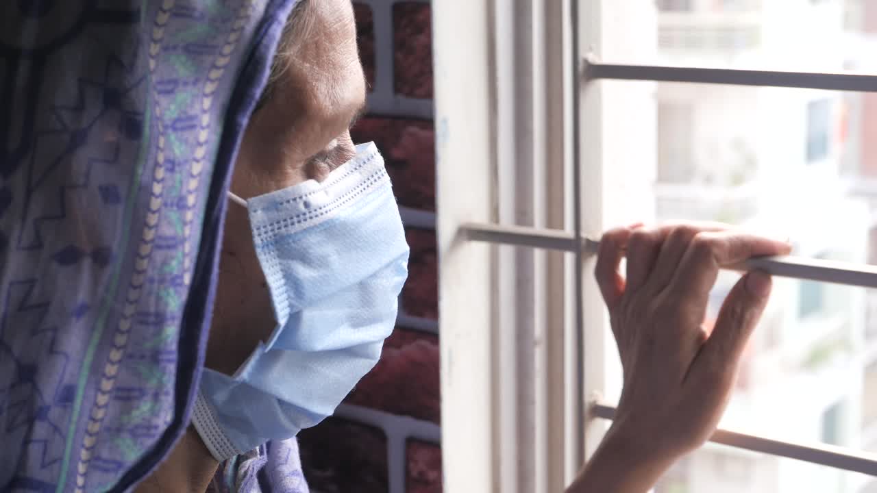 마스크를 착용 한 노인 여성이 창밖을 바라보고 있습니다.