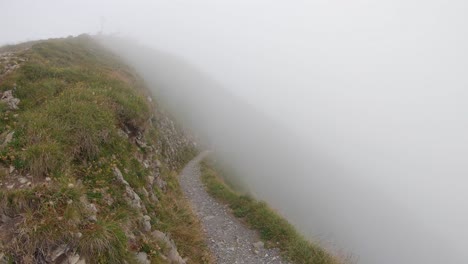 hiking man walks out of the thick fog on narrow trail in alps, switzerland