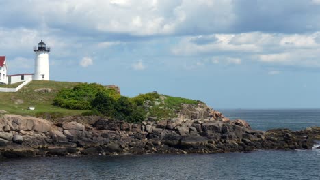 a panning view of cape neddick nubble lighthouse under a blue summer sky with puffy clouds