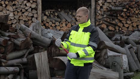 Lumberjack-in-reflective-jacket.-Man-woodcutter-hold-small-axe,-show-ok-sign.-Sawn-logs,-firewood