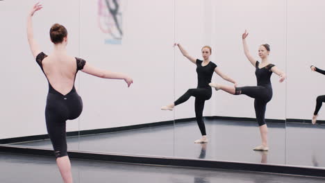 female students at performing arts school rehearsing ballet in dance studio reflected in mirror